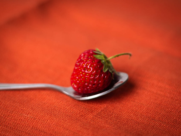 Primer plano de fresa en cuchara sobre fondo rojo
 - Foto, Imagen