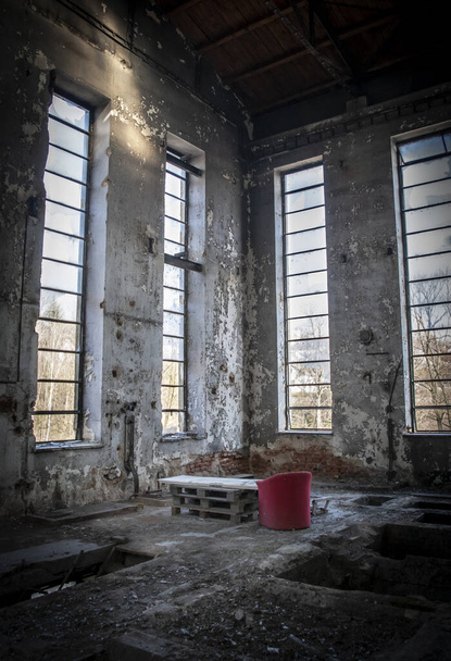 Stara opuszczona fabryka, brudne wnętrze ze starymi czerwonymi krzesłami, nastrojowe jasne światło - Zdjęcie, obraz