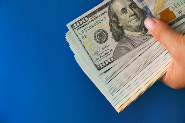 A wad of hundred-dollar bills held in his hand against a bright blue background. The concept of cash, give money on credit, pay in cash - Photo, Image