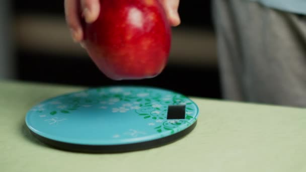 Mies painaa tuoreen punaisen omenan keittiön asteikolla, lähikuva - Materiaali, video
