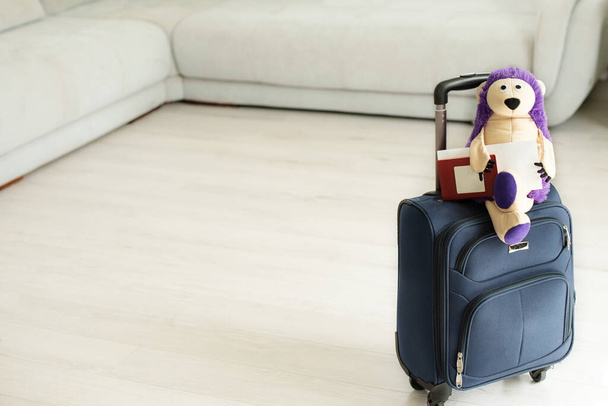 игрушка на чемодане с пальмовыми листьями, домашнее растение. Ежик турист. Упакованный чемодан стоит дома - Фото, изображение