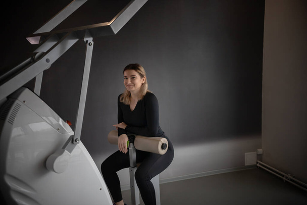 Modern tornaterem - egy fiatal nő ül az erő edzés gép és mosolygós - Fotó, kép