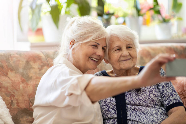 Senior woman and her adult daughter using smartphone together - Fotoğraf, Görsel