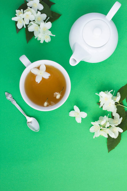 Жасмин зелений чай в білій чашці, чайник і квіти на зеленому тлі, вид зверху, місце для тексту
 - Фото, зображення