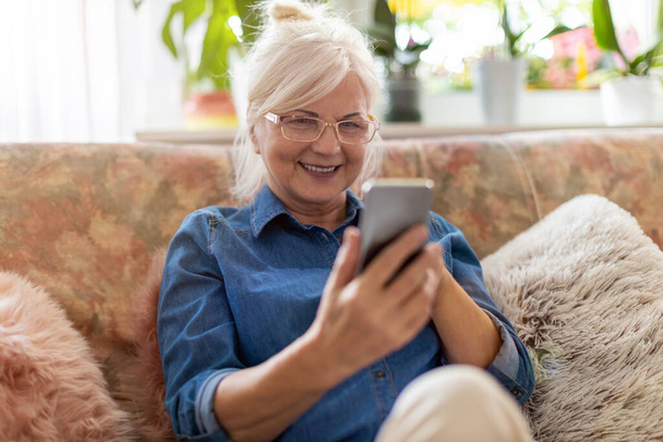 Senior woman using mobile phone at home - Zdjęcie, obraz