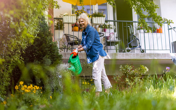 Senior vrouw water geven planten in haar tuin - Foto, afbeelding