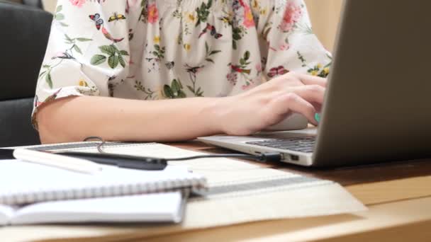 女性はノートパソコンのキーボードに情報を入力し、ノートブックにペンでテキストを書きます - 映像、動画