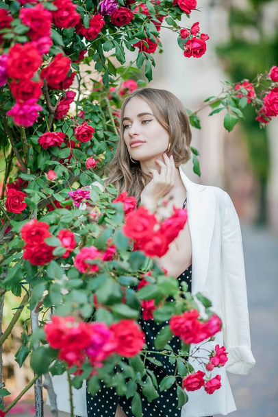 若い美しい女性がヨーロッパの街を歩く。バラの花の近くに若い女性の肖像画。ヨーロッパ. - 写真・画像