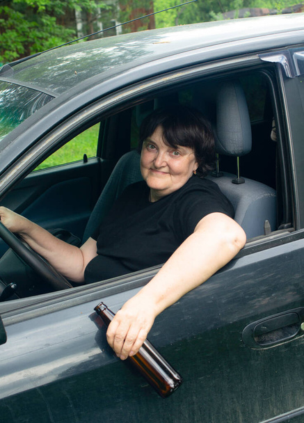 П'яний водій. П'яна літня жінка з пляшкою в руках сидить за кермом машини
 - Фото, зображення
