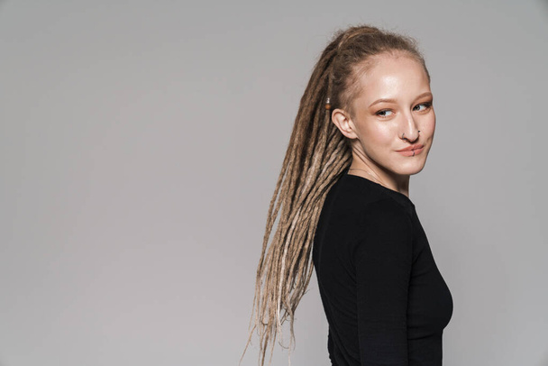 Portrait of an attractive smiling young woman with dreadlocks standing isolated over gray background, posing - Photo, Image