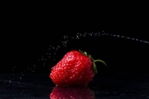 Fresas sobre fondo negro. Foto creativa de fresas. Un chorro de agua está por encima de las fresas. El agua se pega sobre las fresas
.  - Foto, Imagen