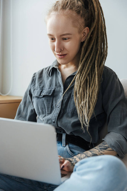 Image of a concentrated young girl with dreadlocks and piercing indoors using laptop computer. - Photo, Image