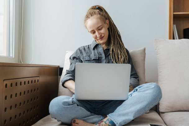 Image of a pleased young girl with dreadlocks and piercing indoors using laptop computer. - Фото, изображение