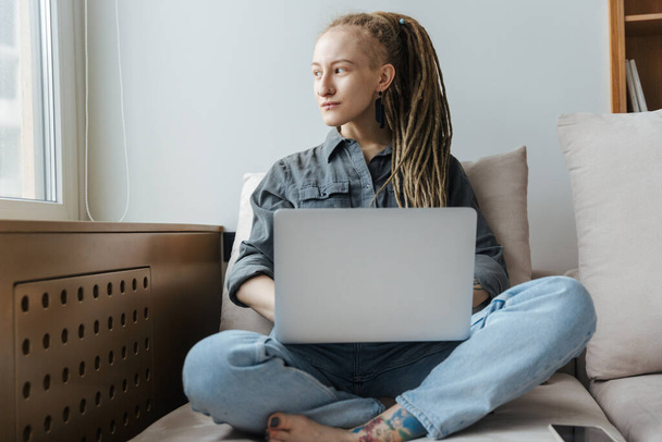 Image of a concentrated young girl with dreadlocks and piercing indoors using laptop computer. - Фото, изображение