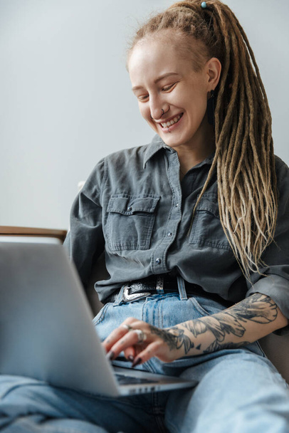 Image of a happy young girl with dreadlocks and piercing indoors using laptop computer. - Φωτογραφία, εικόνα