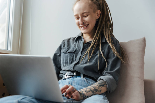 Image of a positive optimistic young girl with dreadlocks and piercing indoors using laptop computer. - Fotografie, Obrázek