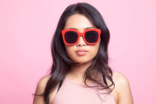 Portrait of a beautiful young asian girl in sunglasses on pink background - Foto, imagen