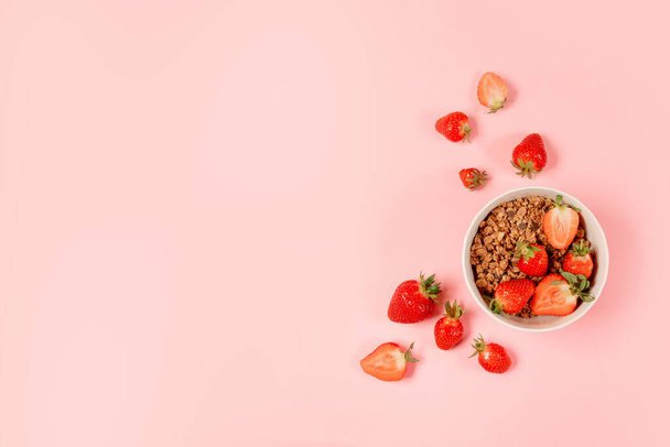 ピンク色の背景に白いボウルにグラノーラ、牛乳、有機おいしいイチゴとトップビューの朝食ボウルコピースペース - 写真・画像