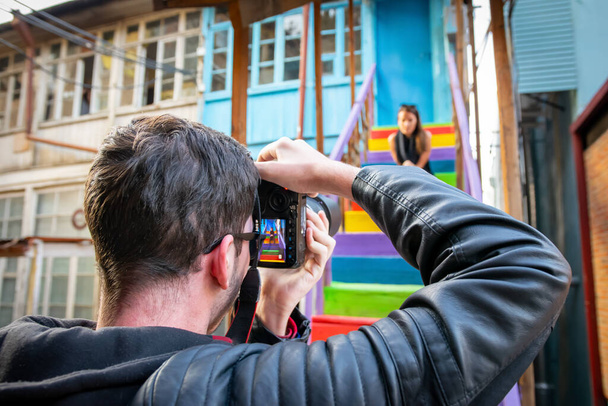 A férfi fotós egy kamerát tart, és egy női lányt fényképez, amint színes lépcsőn ül. Utazási fotózás híres tereptárgyak - Fotó, kép