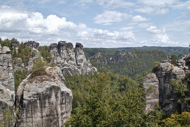 View from the Bastei bridge over the valley called Wehlgrund with the typical sandstone rocks of Saxon Switzerland under a cloudy sky - Fotó, kép