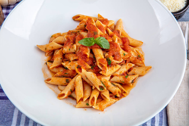 Penne pasta with chili sauce arrabiata. Classic italian penne arrabiata with basil and freshly grated pecorino cheese on a rustic wooden table. - Foto, Bild