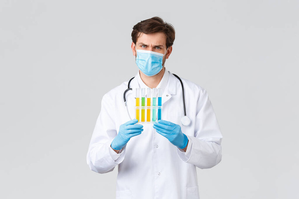 Hospital, healthcare workers, covid-19 treatment concept. Concerned and troubled doctor in medical mask, gloves showing samples of vaccine, studying vaccines, searching treatment coronavirus - Photo, image