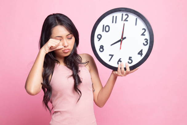 Sleepy young Asian woman with a clock in the morning on pink background - Foto, Imagen