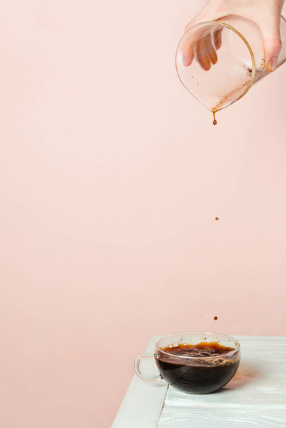 Woman's hand pouring coffee into glass cup on white table, pastel background, copyspace - Photo, Image