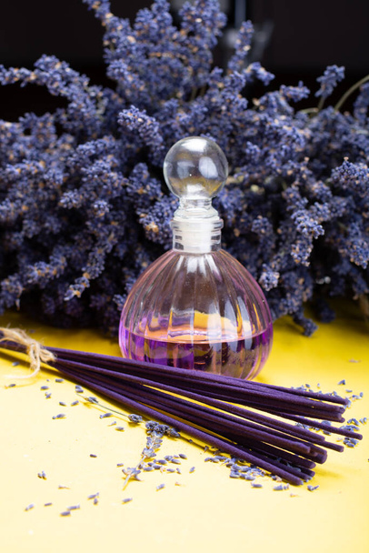 Přírodní zdravá aromaterapie a domácí vůně, fialové levandulové vonné tyčinky a difuzor na žlutém pozadí se sušenými květy levandule zblízka - Fotografie, Obrázek
