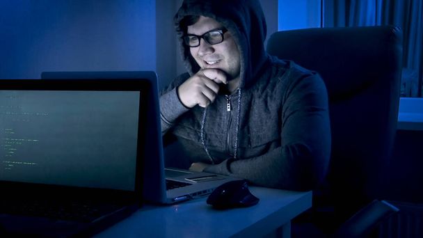 Retrato del hacker masculino sonriente mirando en el ordenador portátil después de robar dinero y hacer delito cibernético
 - Foto, imagen