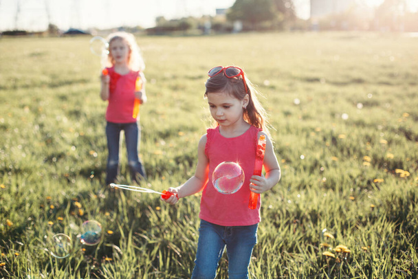 Fogj egy buborékot. A lányok barátai szappanbuborékokat fújnak a parkban a nyári napon. Gyerekek szórakoznak a szabadban. Hiteles boldog gyermekkori varázslatos pillanat. Életmód szezonális tevékenység gyermekek számára. - Fotó, kép