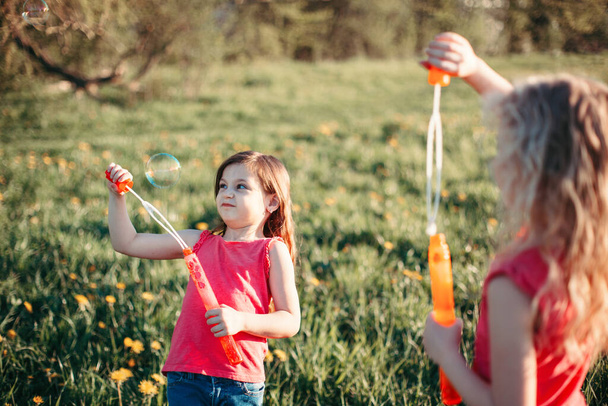 Веселий веселий момент. Дівчата друзі дме мильні бульбашки в парку в літній день. Діти розважаються на відкритому повітрі. Справжній щасливий спосіб життя в дитинстві. Сезонна активність для дітей
. - Фото, зображення
