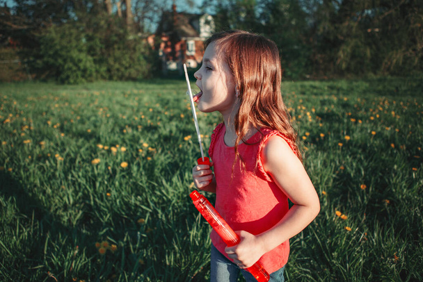 Okul öncesi Kafkasyalı kız yaz günü parkta sabun köpüğü üflüyor. Çocuk dışarıda eğleniyor. Otantik mutlu çocukluk büyülü anı. Çocuklar için yaşam tarzı mevsimsel etkinlik. - Fotoğraf, Görsel