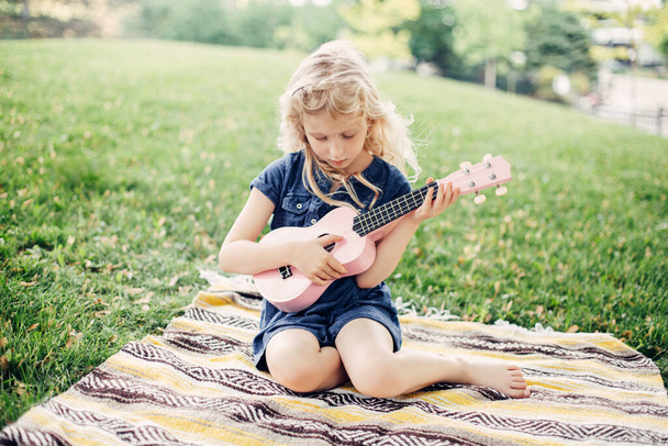 Roztomilé rozkošné blondýny dívka hraje růžovou kytaru hračku venku. Dítě hrající hudbu a zpívající píseň v parku. Koníčková aktivita pro děti. Něžná nezapomenutelná chvíle upřímného dětství.  - Fotografie, Obrázek