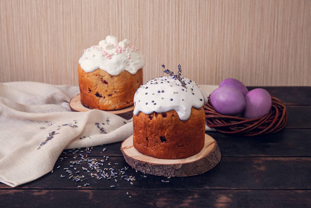 Easter cakes decorated with lavender and marshmallows and painted Easter eggs in a wicker nest On wooden background. - Φωτογραφία, εικόνα