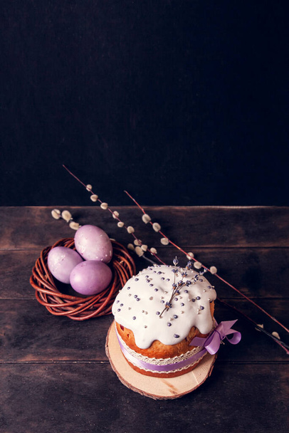 Osterkuchen auf dunklem Hintergrund, dekoriert mit Lavendel und Marshmallows, bemalte Ostereier in einem Weidennest und Weidenzweig - Foto, Bild