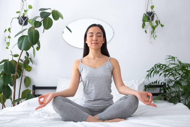 Smiling young pretty woman meditating in bedroom - Photo, image