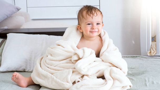 Carino sorridente bambino coperto di asciugamano bianco dopo il bagno seduto sul letto
 - Foto, immagini