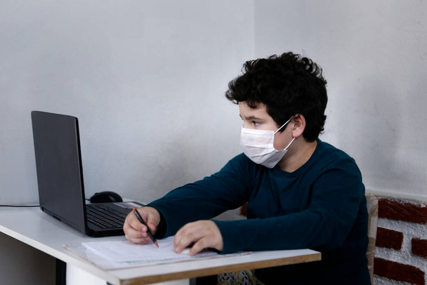Beyaz çocuk bilgisayar ile çalışıyor ve solunum koruma maskesi takıyor. - Fotoğraf, Görsel