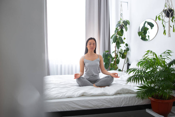 Tranquil young woman in lotus position in bedroom - Фото, изображение