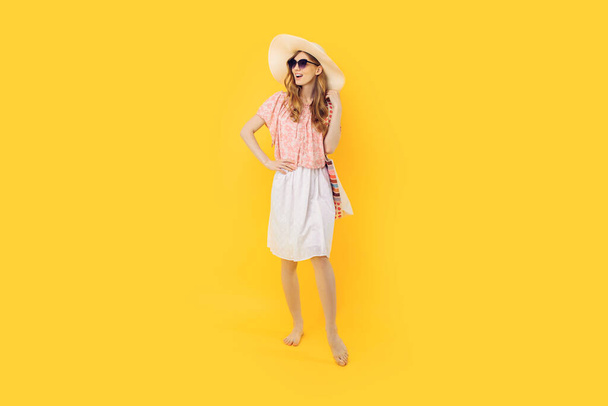 Full length, attractive happy young woman in sunglasses and a summer hat, on an isolated yellow background - Fotó, kép