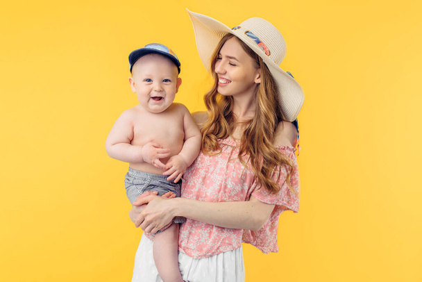Happy young beautiful mother in a summer hat holding a little boy on a yellow background. Summer holidays - Φωτογραφία, εικόνα
