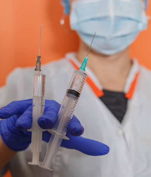 Een arts met een beschermend masker en handschoenen toont een spuit met een vaccin om te werken met de covid-19 coronavirus pandemie tijdens de epidemie - Foto, afbeelding