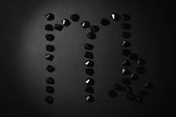 Symbol of the zodiac sign Virgo made by black stones on a black background. Low dark key. Vignetting lighting. Horoscope Theme - Photo, Image