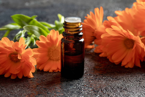 Una botella oscura de aceite esencial con flores frescas de caléndula
 - Foto, imagen