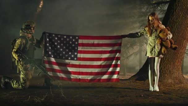 Knielende soldaat in het volledige leger apparatuur en jong meisje met Teddy Bear Toy Holding Amerikaanse vlag en vieren van de overwinning.  - Video