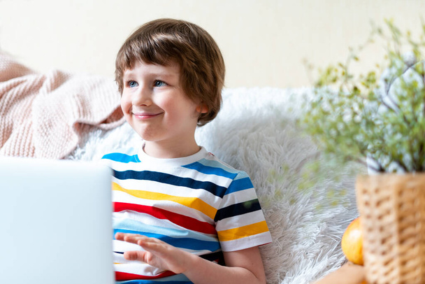 Навчання на відстані онлайн. Хлопчик з Кавказької посмішки вчиться вдома з блокнотом і робить домашнє завдання. Сидячи на дивані та ковдрі з яблуком та комп "ютером. - Фото, зображення