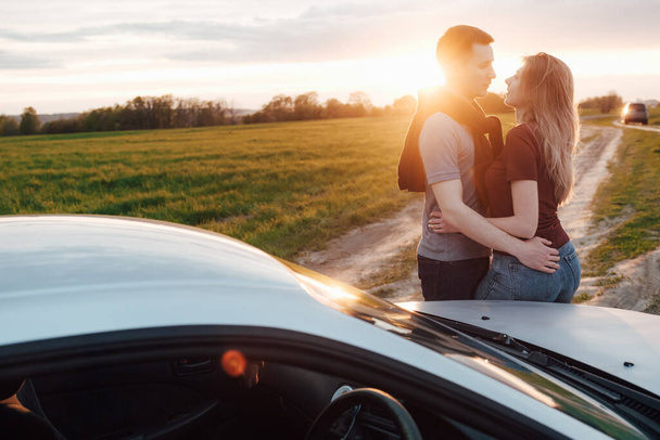 jovem casal elegante amoroso estão andando e se divertindo em um campo de floresta ao pôr do sol amanhecer perto do carro
 - Foto, Imagem