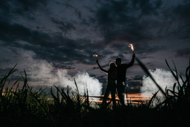young loving having fun couple in a field with fireworks far from all silhouette - Фото, изображение