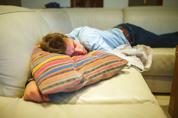 Νεαρός άνδρας αποκοιμήθηκε στον καναπέ, φυσικό φως, εσωτερικό. - Φωτογραφία, εικόνα